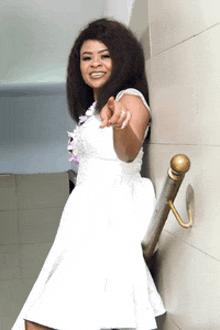 a woman in a white dress is standing next to a railing and pointing at the camera