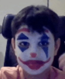 a young boy is wearing a clown makeup on his face .