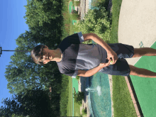 a young man stands in front of a golf course with a fountain in the background