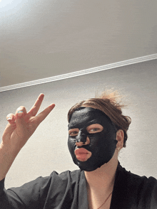 a woman wearing a black mask on her face giving a peace sign