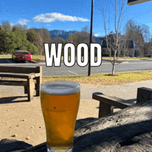 a glass of beer sits on a wooden table in front of a sign that says " wood "