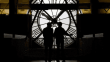 two men are standing in front of a large clock tower .