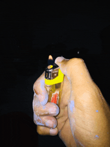 a hand is holding a yellow lighter with a black top