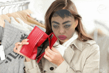 a woman with makeup on her face holds a red wallet