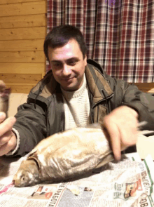 a man sits at a table with a fish on top of a newspaper that says " pe rabota " on it