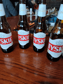 four bottles of tyskie beer are lined up on a wooden table