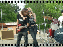 a man playing a guitar and a woman singing in front of a drum set that says later on it