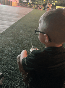 a young boy wearing glasses is sitting on the grass eating ice cream