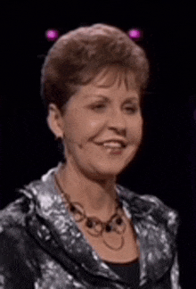 a woman wearing a necklace and a jacket is smiling and looking at the camera .