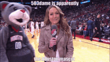 a woman talking into a microphone next to a houston mascot on a basketball court