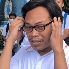 a man wearing glasses and a white shirt adjusts his hair