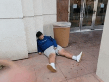 a person is laying on the ground next to a trash can .