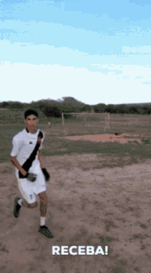 a man in a white shirt and shorts is running on a dirt field with the word receba written below him