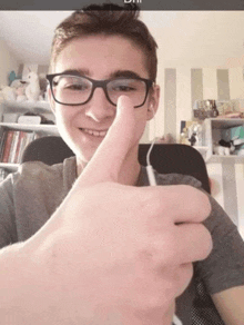 a young man wearing glasses giving a thumbs up sign