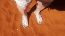 a woman 's feet in flip flops are standing on a sandy surface