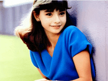 a young girl in a blue dress leans against a wall