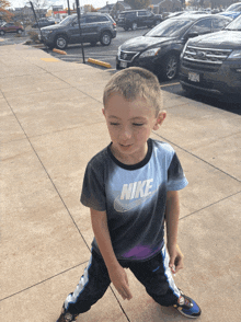 a young boy wearing a nike t-shirt is standing on a sidewalk