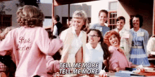 a group of women are standing around a table talking to each other . one of the women is wearing a pink shirt .