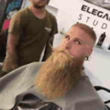 a man with a beard is getting his hair cut by a barber in a barber shop .