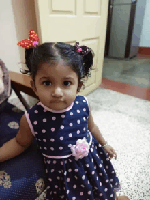 a little girl wearing a blue polka dot dress with a pink flower on the waist