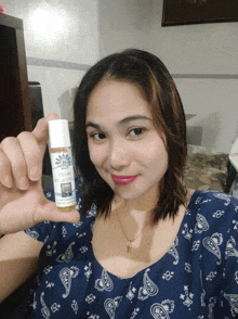 a woman in a blue paisley shirt is holding a small bottle of essential oil in her hand