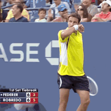 a man in a yellow shirt is holding a tennis racquet in front of a sign that says 1st set tiebreak