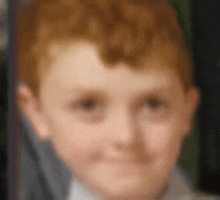 a close up of a young boy 's face with red hair and a white shirt .