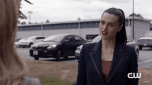 a woman in a suit is talking to another woman in a parking lot with cars parked behind her .