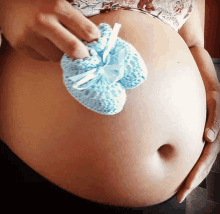 a pregnant woman is holding a pair of blue baby booties on her belly