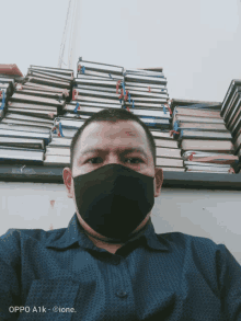 a man wearing a black face mask is sitting in front of a stack of books