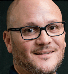 a bald man with glasses and a beard smiles at the camera