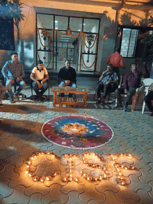 a group of men sit around a table in front of a building with candles in the shape of the letter o