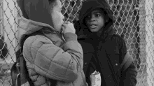 a black and white photo of two children standing next to a chain link fence one of the children is holding a box of french fries