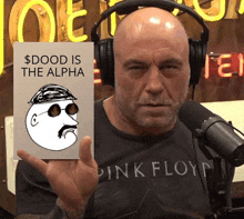 a man wearing headphones and a pink floyd shirt holds up a card that says " dood is the alpha "