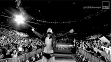 a wrestler is walking out of a ring with his arms outstretched in front of a crowd of people .