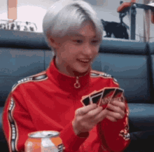 a young man in a red jacket is playing a game of uno and smiling .