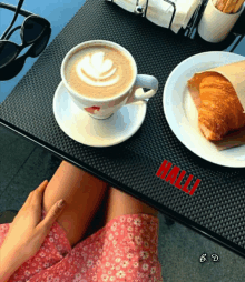 a woman in a pink dress sits at a table with a cup of coffee and a plate of croissant