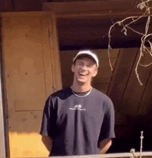 a man wearing a hat and a black t-shirt is laughing while standing in front of a wooden door .