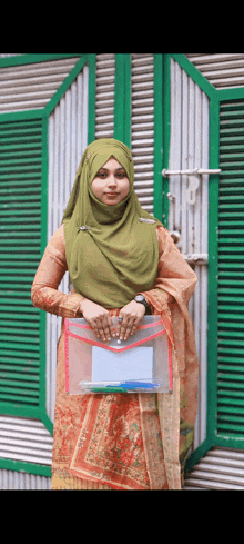 a woman wearing a green hijab holds a clear envelope