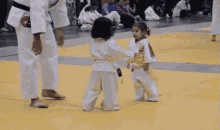 a person in a white kimono is standing next to a child in a white kimono on a wrestling mat .