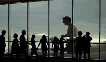 a group of people are standing in front of a large window with a man standing in the background