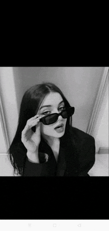 a black and white photo of a girl wearing sunglasses and a black jacket .