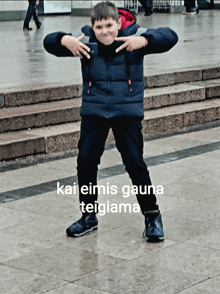 a boy in a blue jacket is standing in front of stairs with the words kai einis gauna teigiama written on the ground