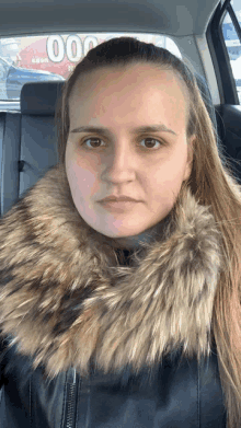 a woman wearing a fur collar is sitting in a car in front of a sign that says 000