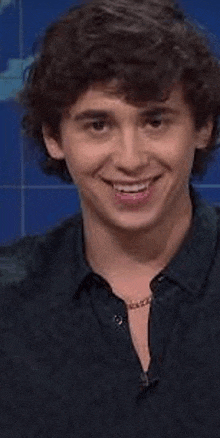 a young man with curly hair is smiling while wearing a black shirt and a necklace .