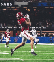 a football player catches a ball while wearing a red uniform with the number 5 on it