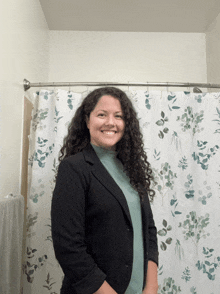 a woman in a black jacket smiles in front of a shower curtain with leaves on it