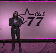 a man in a black suit stands in front of a club 77 sign