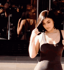 a woman in a black tank top holds her hair in front of a store window