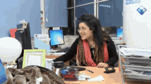 a woman sits at a desk in front of a computer with a sign on the wall that says ' microsoft ' on it